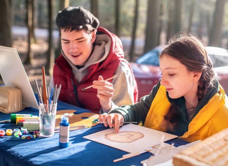 Two people painting outdoors on table.